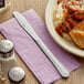 A Choice stainless steel dinner knife on a napkin next to a plate of food.