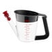 A clear plastic measuring cup with red text and a black and red handle.
