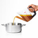 A hand using an OXO Good Grips fat separator to pour brown liquid into a pot.