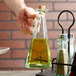 A hand pouring olive oil into a Tablecraft Marbella glass cruet.