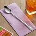 A Choice stainless steel iced tea spoon on a napkin next to a glass of ice tea.