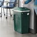 A woman putting paper in a green Rubbermaid Slim Jim trash can.