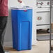 A man standing next to a Rubbermaid blue square recycling container.