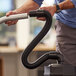 A man using a ProTeam vacuum tube with black cuffs to clean a floor.