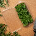 A clear CKF container of parsley next to a knife on a cutting board.