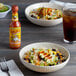 A bowl of rice and beans with Cholula Chili Garlic Hot Sauce on a table.