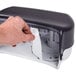 A hand opening a San Jamar Versatwin double roll toilet tissue dispenser.