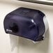 A black San Jamar Versatwin double roll toilet paper dispenser holding one roll of toilet paper.