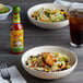 A bowl of food with Cholula chili lime hot sauce on a table.