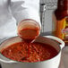 A person pouring Cholula Chipotle hot sauce into a pot.