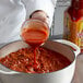 A person pouring Cholula Original hot sauce into a pot of food.