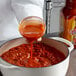 A person pouring Cholula Chili Garlic hot sauce into a pot.