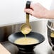 A hand using a Vollrath Jacob's Pride stainless steel ladle to pour soup into a bowl.