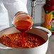 A person pouring Cholula chili lime hot sauce into a pot.