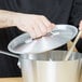 A person using a Vollrath Arkadia lid to cover a pan with a spoon inside.