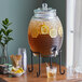 A Libbey beehive glass beverage dispenser filled with liquid, lemons, and ice on a table.