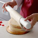 A person using Satin Ice ChocoPan to cover a cake with ivory chocolate.