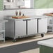 A stainless steel three-door worktop refrigerator on wheels, designed for commercial kitchen use.