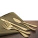 A close-up of a Walco Colgate gold stainless steel table fork and spoon on a napkin.