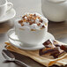A white cup of HEATH Cappuccino with whipped cream and chocolate chips on a saucer.