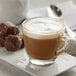 A glass cup of UPOURIA hot chocolate with white foam on top.