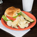 A Carlisle Sunset Orange melamine plate with a croissant sandwich, potato chips, and a white cup on a table.