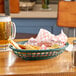 A Tablecraft forest green jumbo oval fast food basket on a table with a bowl of nachos and a glass of beer.