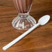 A clear glass of chocolate milkshake with a white Dart plastic spoon.