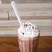 A glass of chocolate milkshake with whipped cream and a white plastic spoon.