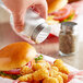 A hand pouring salt from an Acopa mini mason jar onto a burger.