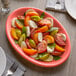 A Tuxton Cinnebar oval china coupe platter with tomatoes and mozzarella on a table.