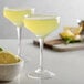 Two Arcoroc Tall Coupe Cocktail glasses filled with yellow drinks and garnished with lemon slices on a table.