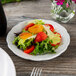 A Tuxton Chicago bright white china plate with salad, strawberries, and tomatoes.