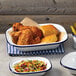 A white rectangular bowl with a blue rim filled with fried chicken next to a white rectangular bowl with a blue rim filled with corn.
