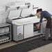 A woman using an Avantco refrigerated pizza prep table to put food into a refrigerator in a professional kitchen.