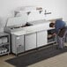 A man putting food into a large Avantco refrigerated pizza prep table.