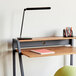 A Safco black LED desk lamp with a multi-pivot adjustable arm and USB port on a desk with notebooks.