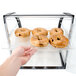 A hand reaching into a Cal-Mil black iron bakery display case to pick up a bagel.