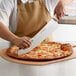 A person using a Dexter-Russell Sani-Safe pizza knife with a white handle to cut a pizza.