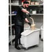 A man wearing black gloves pouring liquid into a white Cambro ingredient storage bin on a white cart.