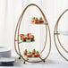 An American Metalcraft 3 tier gold oval stand with frosted glass plates holding food on a table.