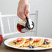 A person using a Tablecraft Modern Glass Syrup Dispenser to pour syrup on a plate of waffles with strawberries and blueberries.