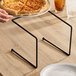 A hand holding a pizza on an American Metalcraft black rubberized pizza stand.