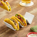 A person holding a taco in a white American Metalcraft taco holder.