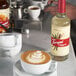 A close-up of a white cup of coffee with Torani Puremade Vanilla syrup on the table.