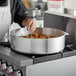 A chef using a Choice aluminum brazier to cook food on a stove.