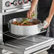 A person cooking food in a Choice heavy-duty aluminum brazier on a stove.