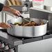 A person cooking food in a Choice aluminum brazier on a stove.