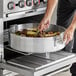 A person cooking food in a Choice aluminum brazier.