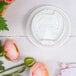 A white table with a Dart white coffee cup with a reclosable tab next to pink flowers.